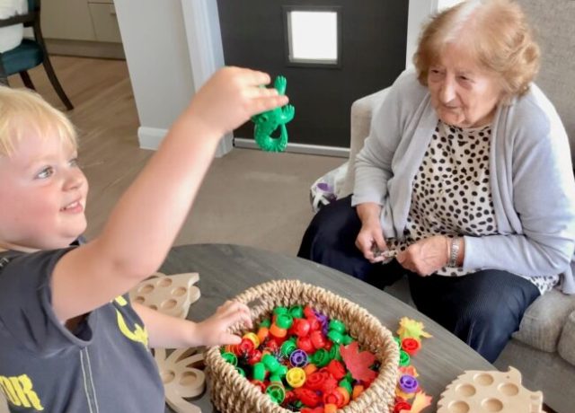 Care home resident enjoying an intergenerational activity with a young child using colourful toys.